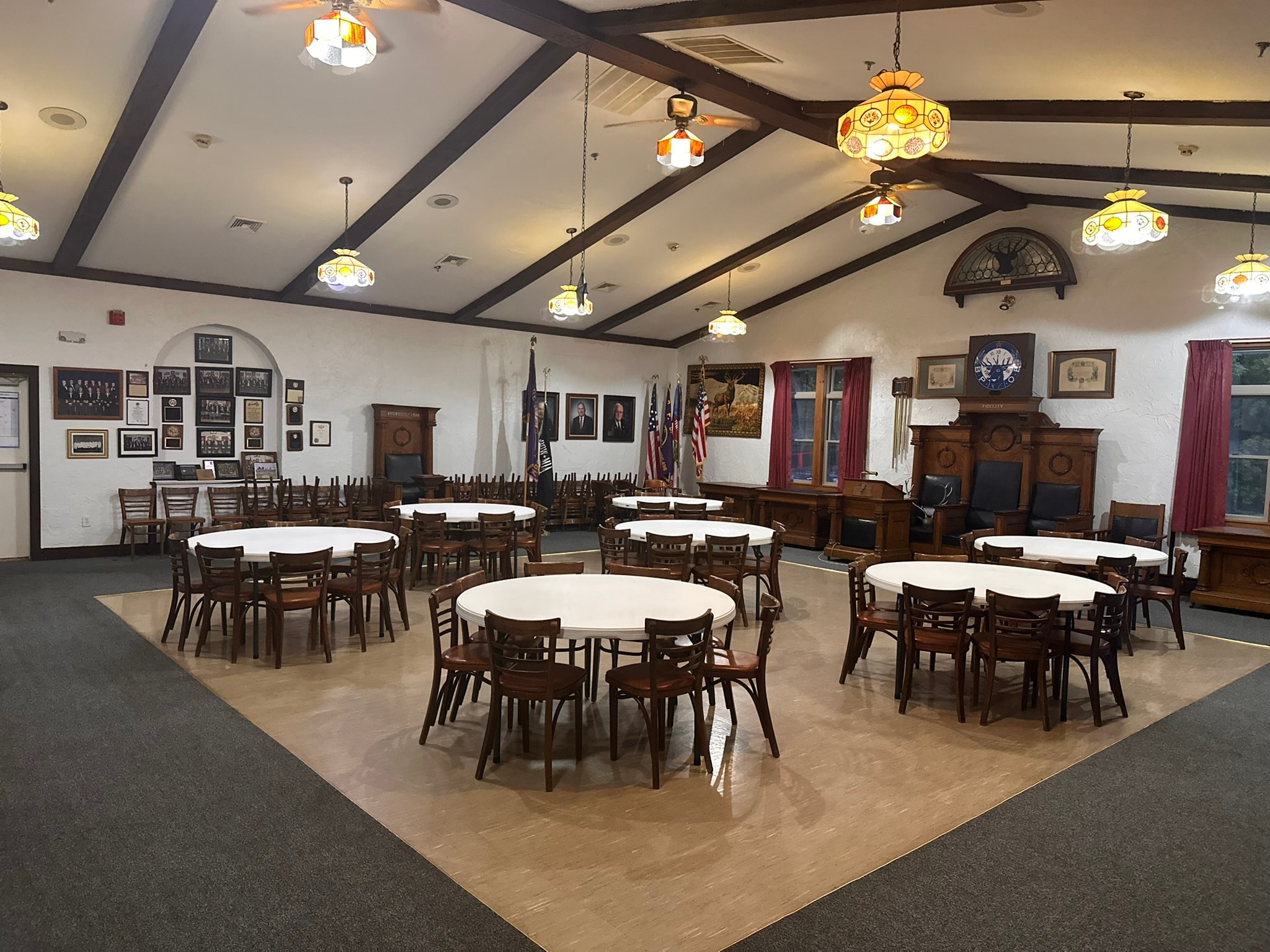 Watertown Elks Lodge meeting room with round tables, dark wood chairs, Tiffany-style pendant lights, and lodge memorabilia on the walls