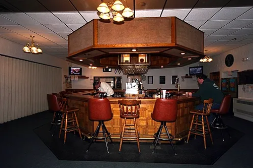 Watertown Elks Lodge Social Parlor Room circular bar with wood paneling, red leather stools, and HDTVs